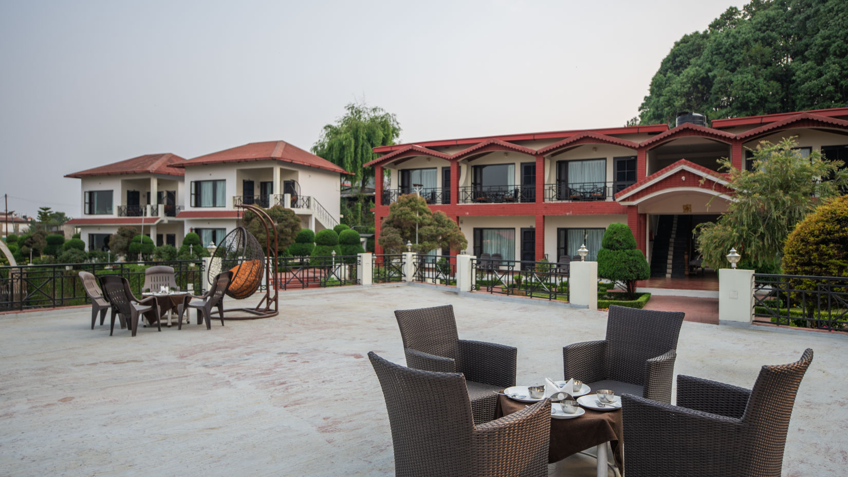 Aerial view of a sprawling luxury resort with several red-roofed stone cottages nestled on a green hillside in the Himalayas.