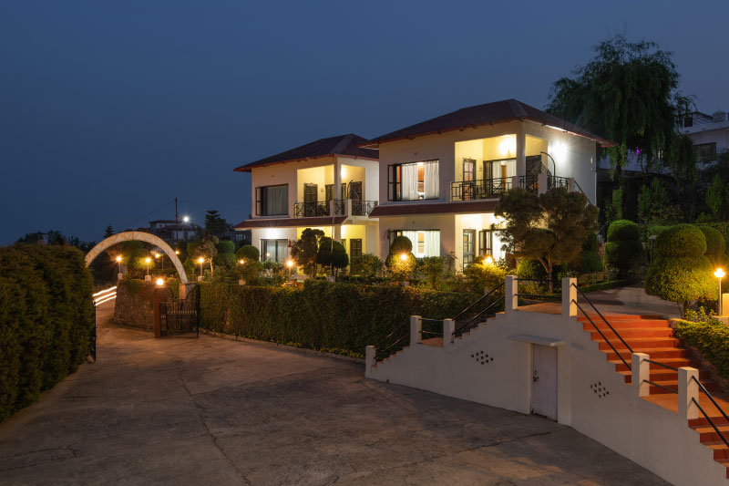 A guest relaxing with a hot drink by a large window in a sophisticated room at Ojaswi Himalayan Resort, enjoying the scenic mountain view.