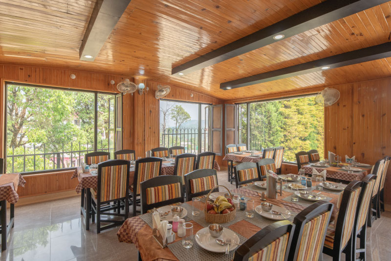 A guest enjoying a relaxing poolside breakfast featuring fresh fruit and classic Kumaoni gourmet cuisine at Ojaswi Himalayan Resort.