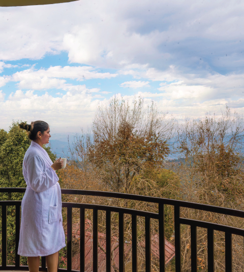 Guest enjoying a peaceful morning coffee on the balcony at Ojaswi Resort in Mukteshwar with scenic Himalayan views